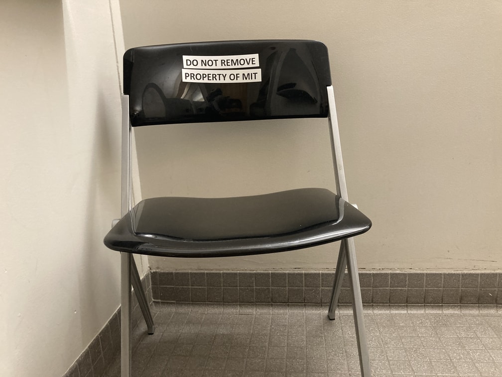 Black folding chair in corner of restroom.