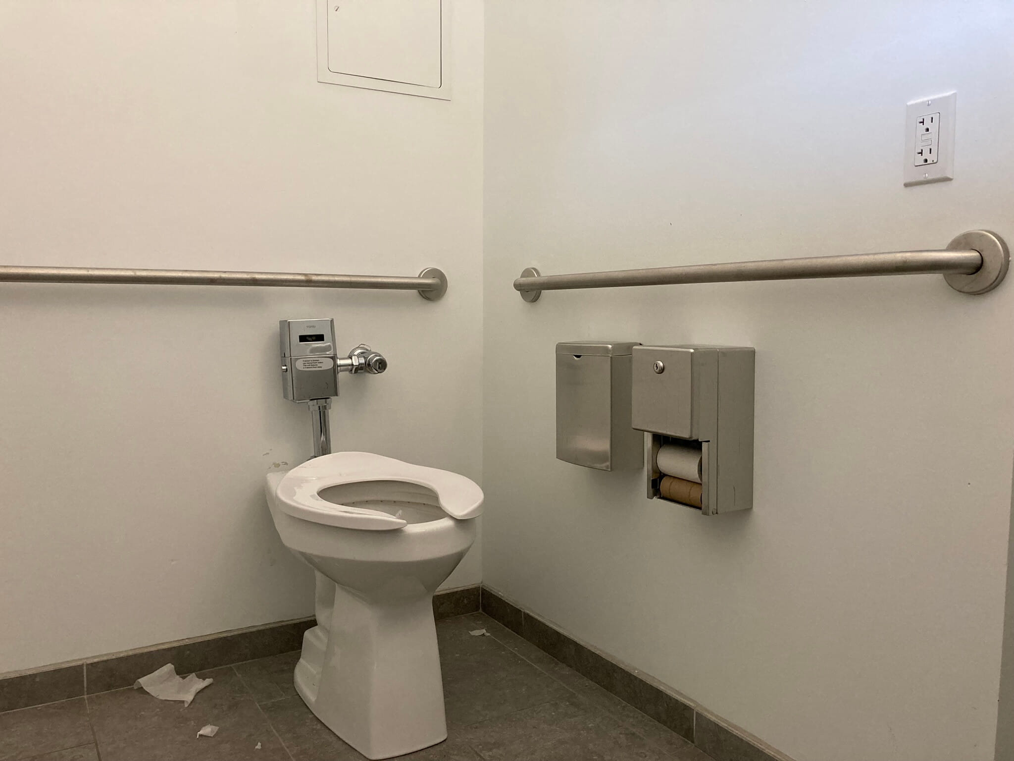 An image of a toilet with some toilet paper on the floor around it.